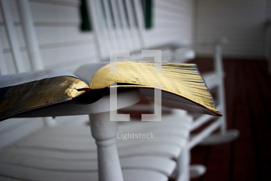 A Bible laying open on the arm of a white rocking chair.