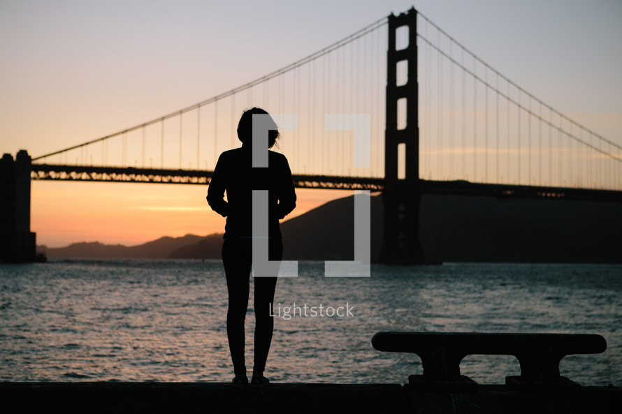 Silhouette of a woman looking at a suspension bridge.
