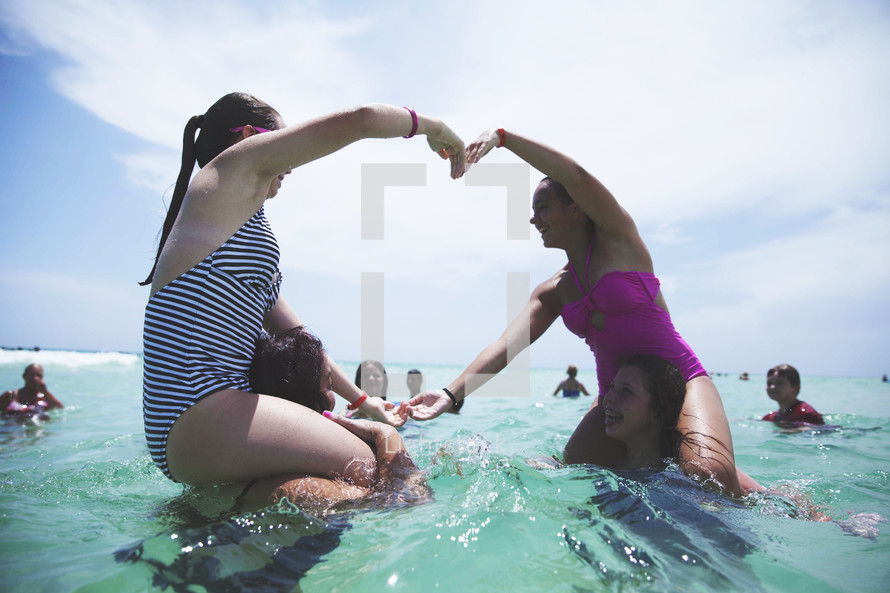 teen girl swimming in the ocean making a heart with their arms 