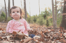 a toddler girl sitting in fall leaves 