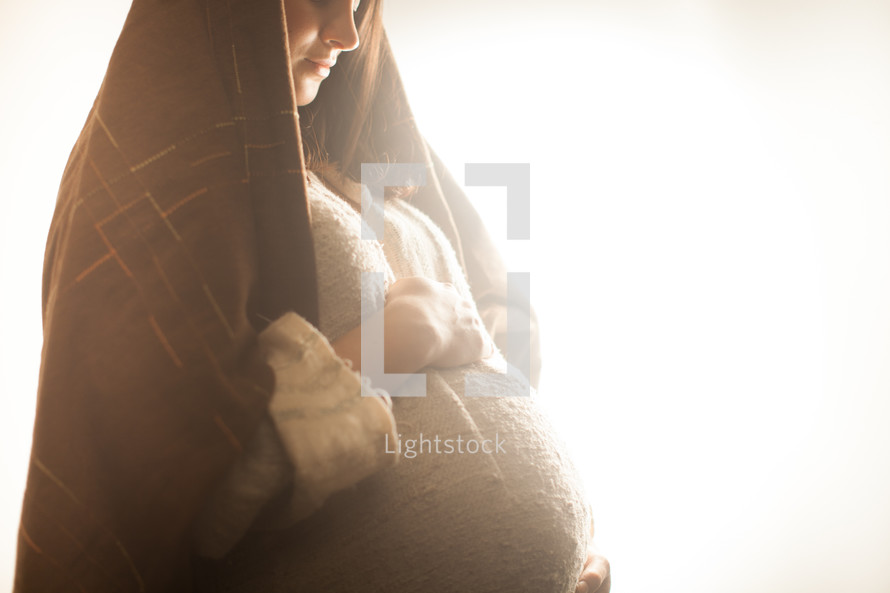 pregnant Mary holding her belly standing in glowing light 