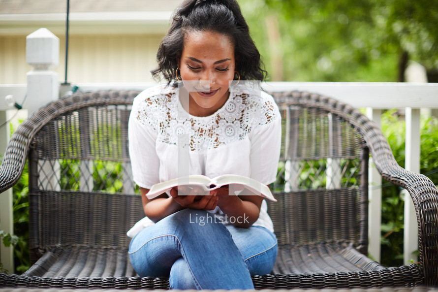 a woman reading a Bible on a porch 