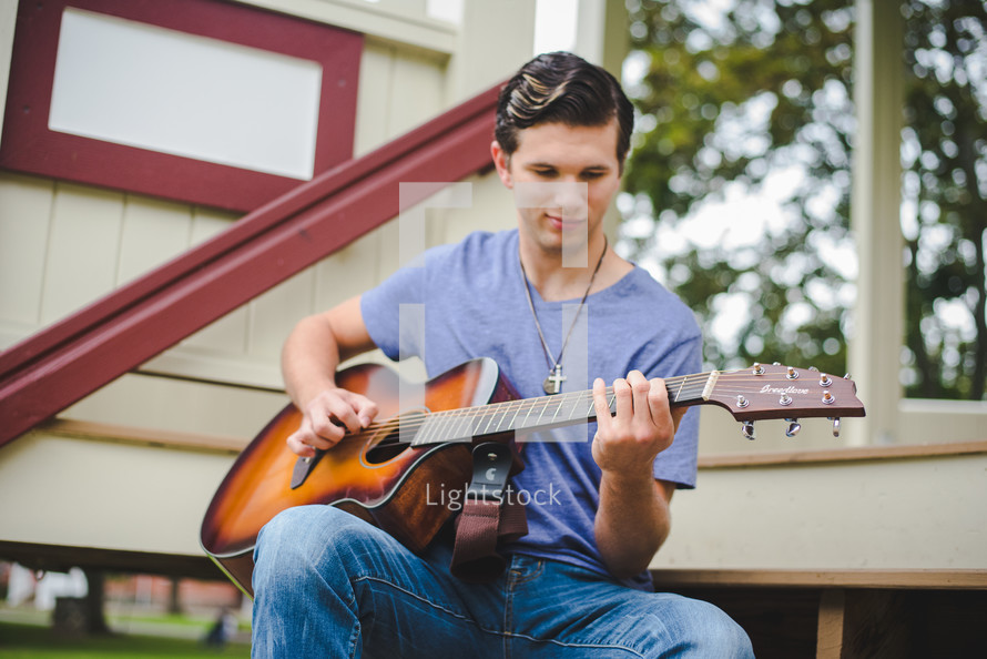 A young man plays a guitar outside.