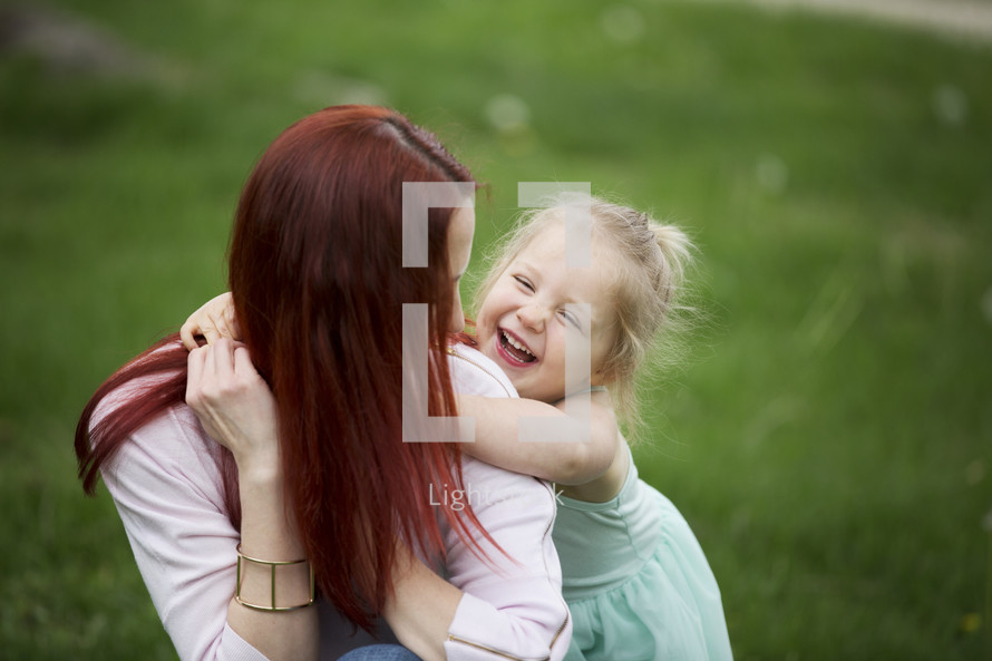 A laughing little girl with her arms around her mother.