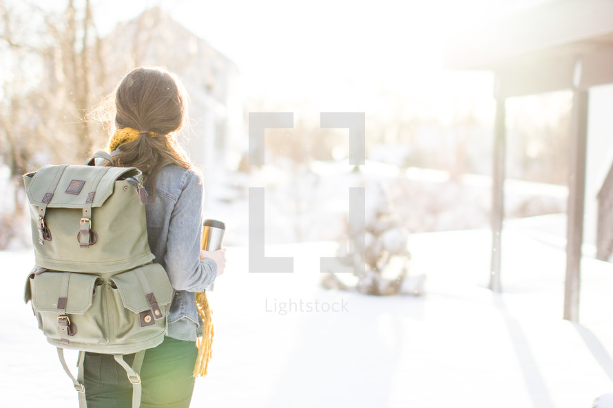 Woman with backpack facing a snow-covered day.