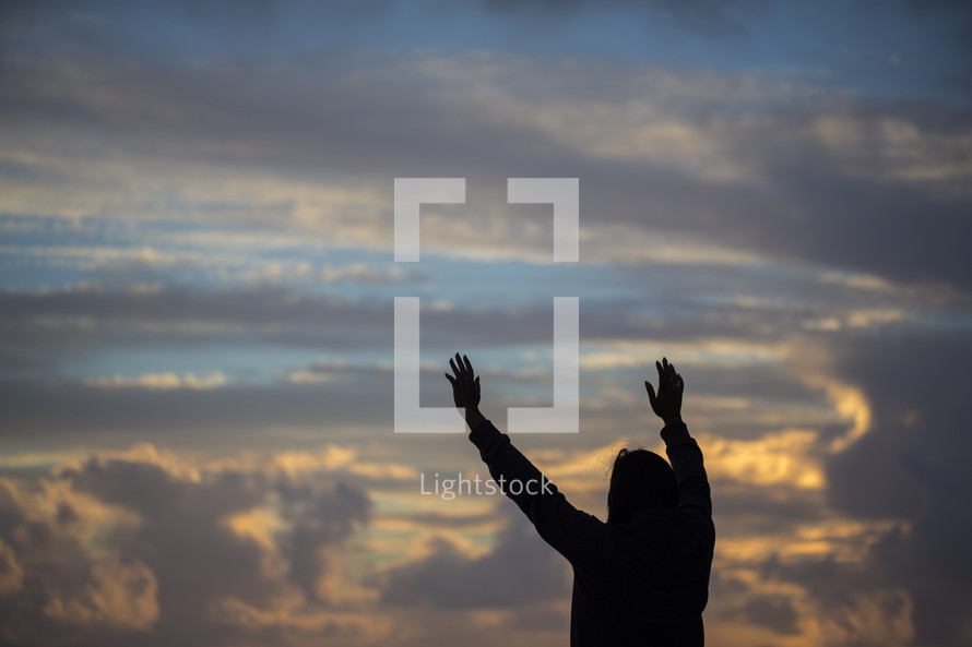 silhouette with raised hands on a beach at sunset 