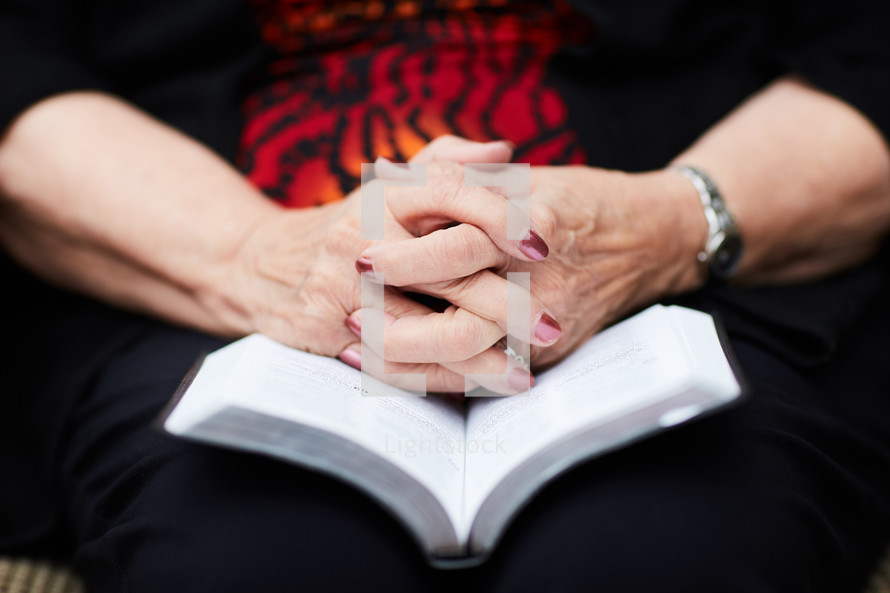 elderly woman with praying hands over a Bible 