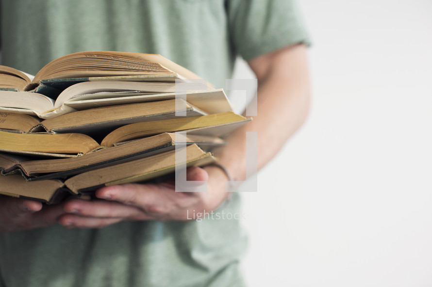 man holding open books stacked in a pile