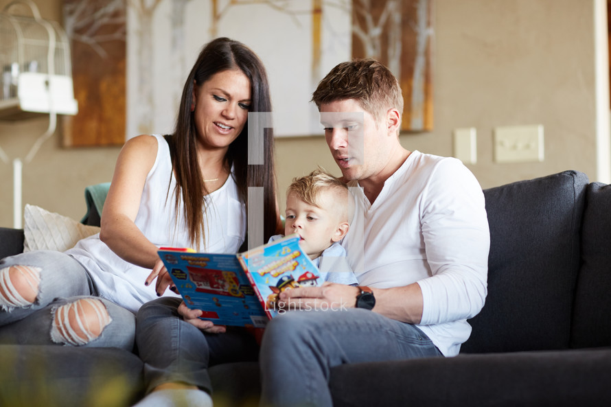 a mother and father reading a children's book to their kids on the couch 