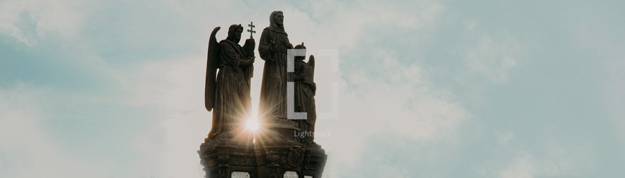 Sculptures of St. Francis Of Assisi - Father Of Mendicant Orders with guardian angels in Prague on Charles Bridge. Blue clear sky. Copy space, banner. Religion, God, faith concept.