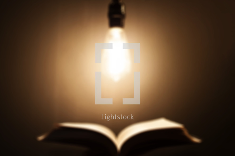 defocused image of an Edison bulb hanging over an open Bible.