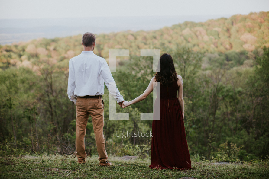 couple holding hands standing on a hill 