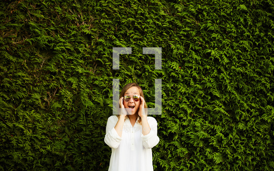 a woman with Ray Bans sunglasses standing in front of a wall of ivy
