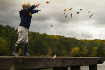 child throwing fall leaves in to a river 