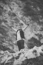man standing on rock with hands raised in worship 