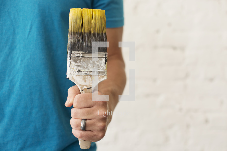 A married man holding a paint brush with yellow paint.