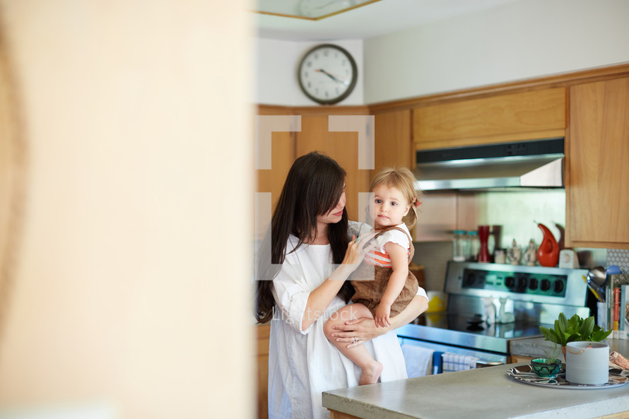 a mother holding her daughter in a kitchen 