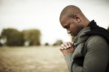 An African American man praying with hands laced