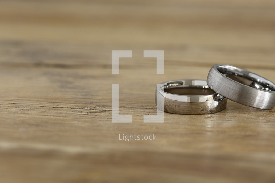 Two men's wedding rings on a wooden table.