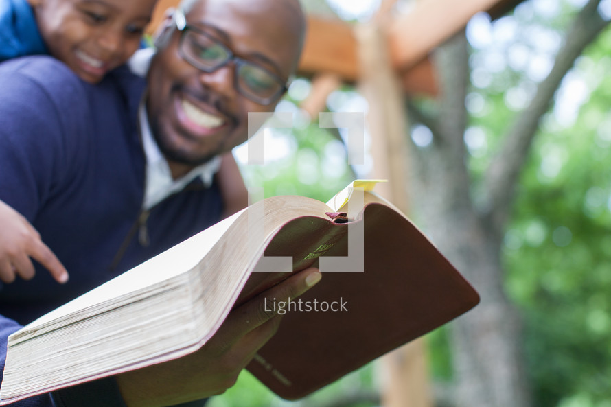 A smiling father and young son reading the Bible.