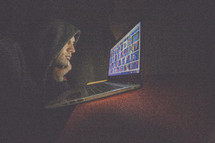A man in a hooded sweatshirt working intently on a laptop computer.