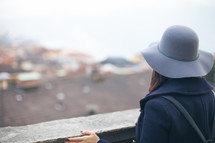 a woman in a coat and hat looking over a railing 