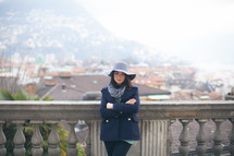 a woman in a peacoat and hat with view of a European town n the background 