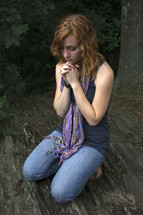 Girl on her kneews praying by a tree.