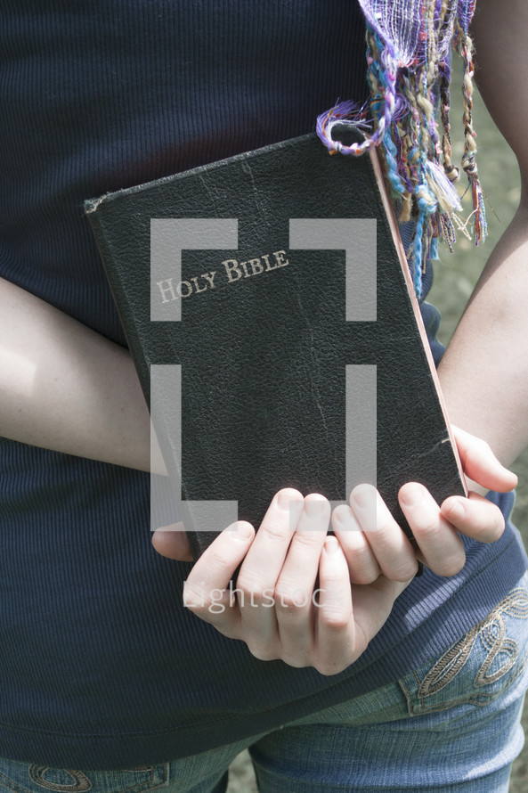 Teen girl holding Bible behind her back.