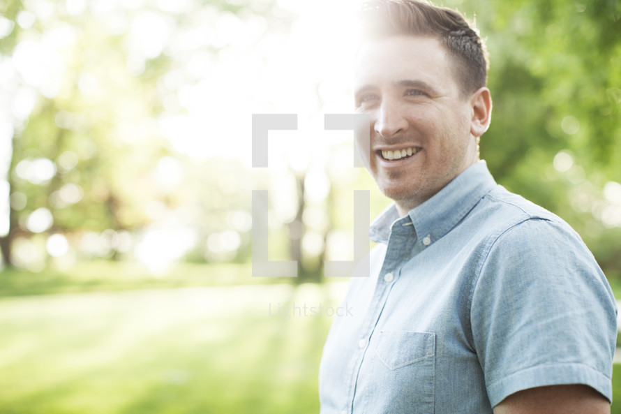 smiling man standing outdoors with natural sun flare. 