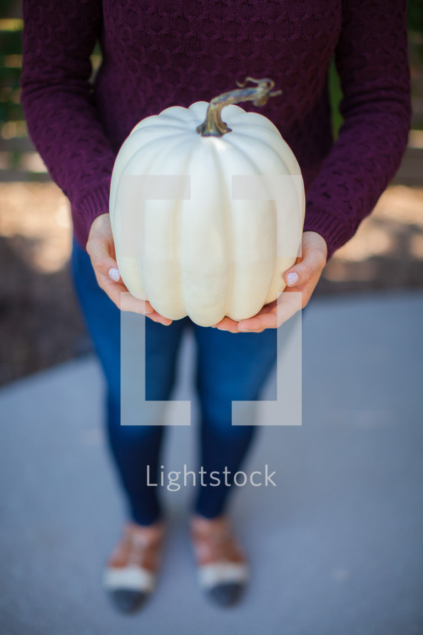 a woman holding a white pumpkin 