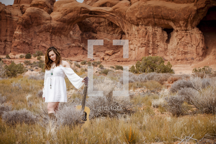 woman with a guitar in front of red rock cliffs