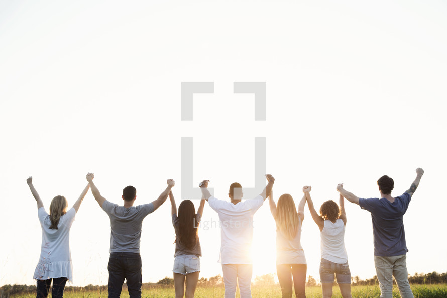 group of young adults standing holding raised hands in worship outdoors 