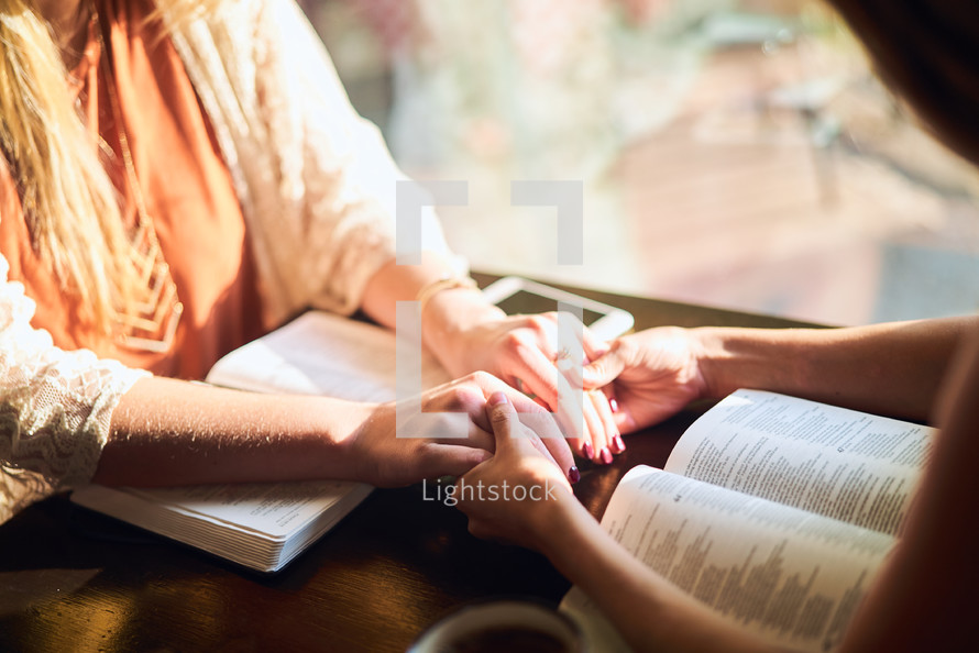 women holding hands in prayer over Bibles 