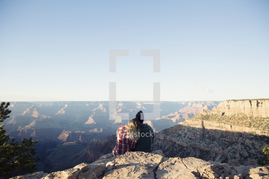 couple sitting at the top of a canyon cliff snuggling 