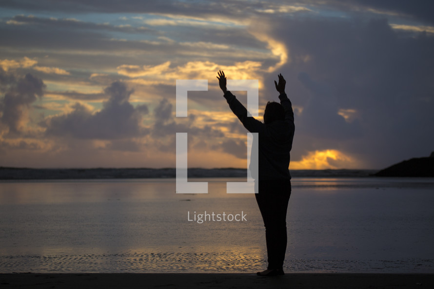 silhouette of a woman with raised hands on a beach 