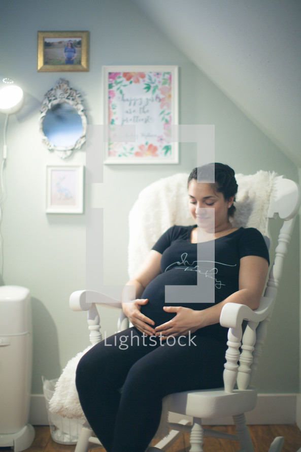 a pregnant woman holding her belly sitting in a rocking chair 