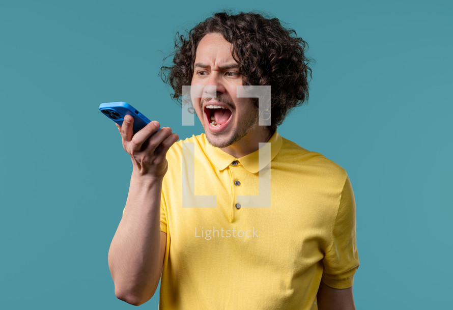 Annoyed young man quarreling while talking on mobile phone. Angry dude, stress. Blue studio background. Conflict, dispute, negative. High quality