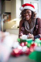 A smiling woman wearing a santa hat and wrapping Christmas presents