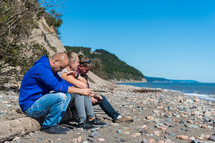 three men sitting on a shore 