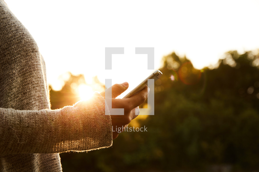 a woman holding her cellphone outdoors in sunlight 