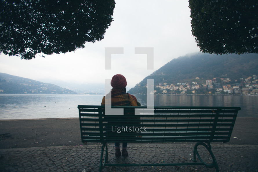 woman sitting on a park bench looking out over a waterway 