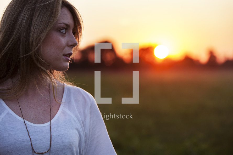 side profile of a young woman standing outdoors at sunset 
