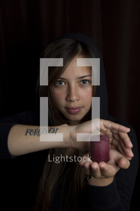 woman with a tattoo of the word Forgiven on her arm holding a candle