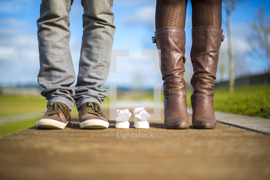 feet of a mother and father and baby shoes 