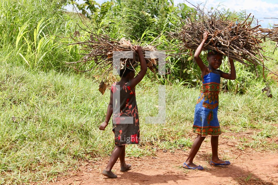 children carrying sticks over their heads 