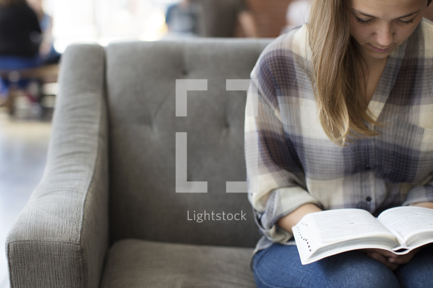 woman sitting on a couch reading a Bible in a coffee shop.