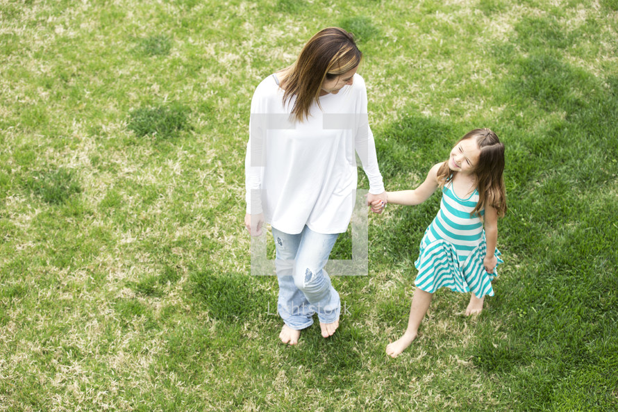 mother and daughter walking holding hands through grass