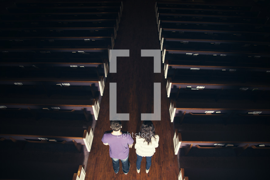 Couple standing int he aisle of a dark ,empty church.