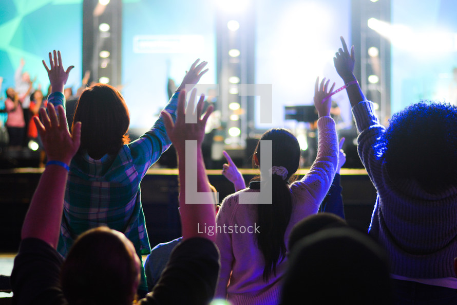 girls standing with raised hands at a worship service 